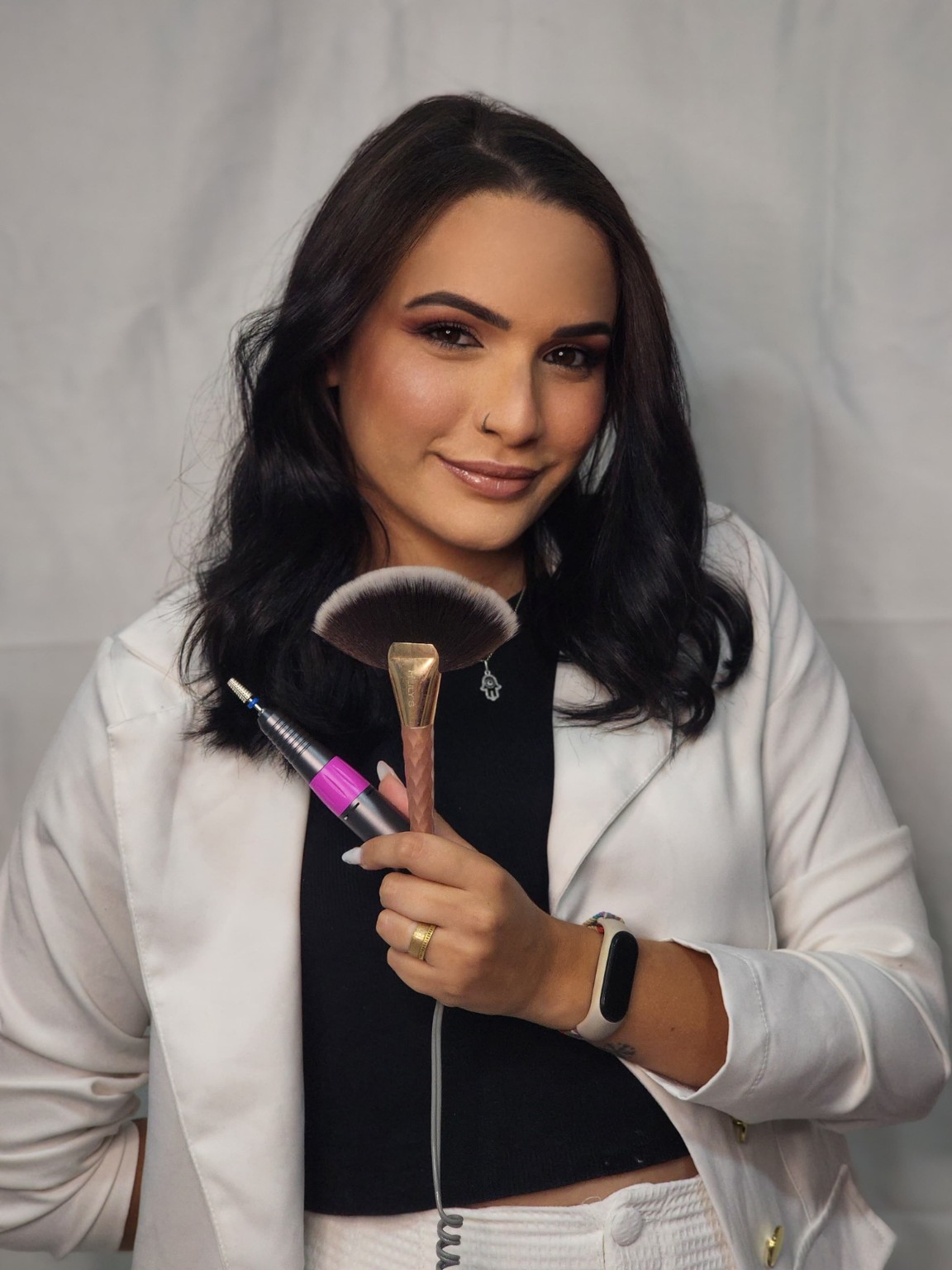 Profissional de unhas e maquiagem, de colete branco com pincéis nas mãos